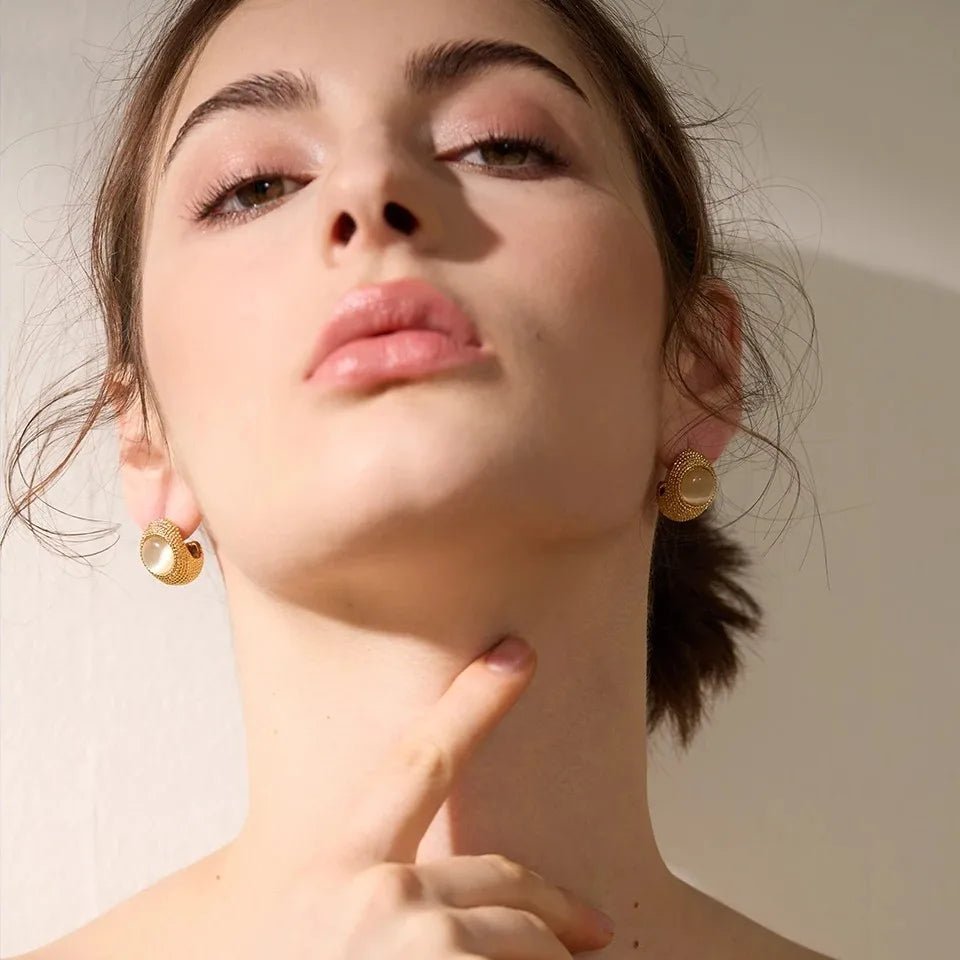 Close-up of a person wearing gold earrings against a neutral background