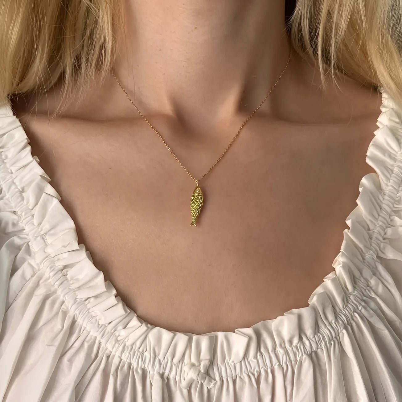 Gold necklace with a leaf pendant worn by a person in a white dress.