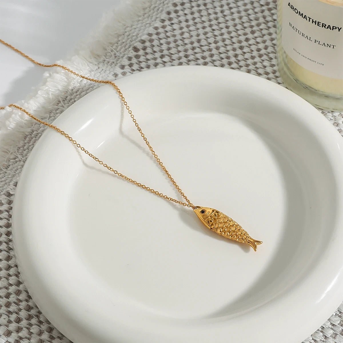 Gold fish-shaped necklace on a white plate with a candle in the background