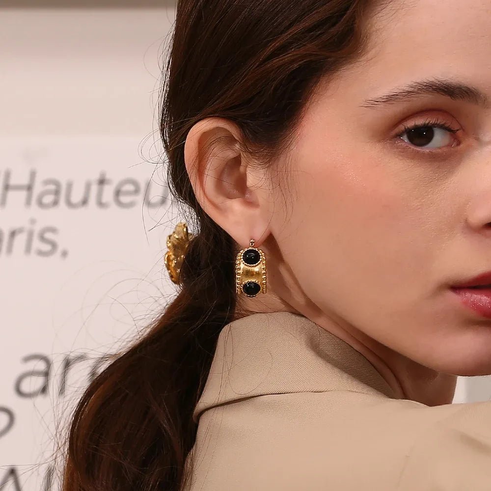 Close-up of a woman wearing gold earrings with black stones, with a blurred background.