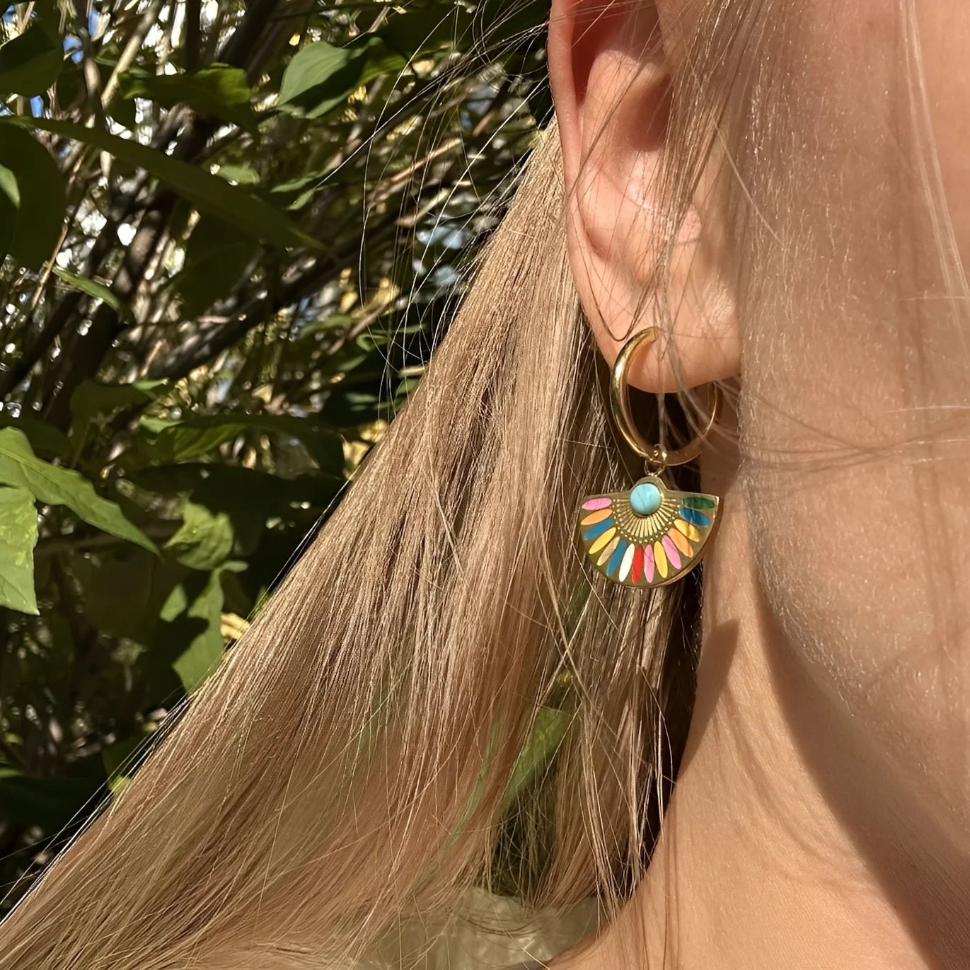 Close-up of a colorful earring worn by a person with blonde hair against a natural background.