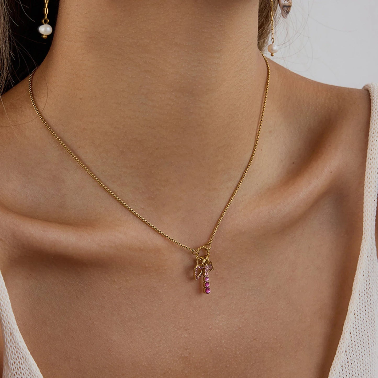 Gold necklace with a pink gemstone pendant on a person wearing a white sleeveless top.