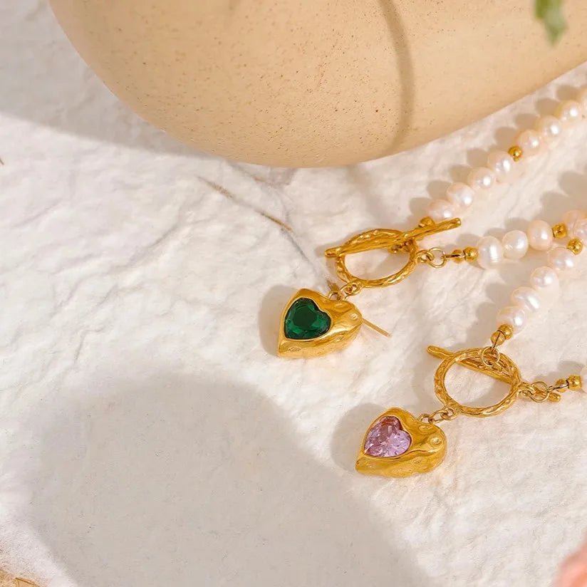 Gold heart-shaped earrings with gemstones on a textured surface