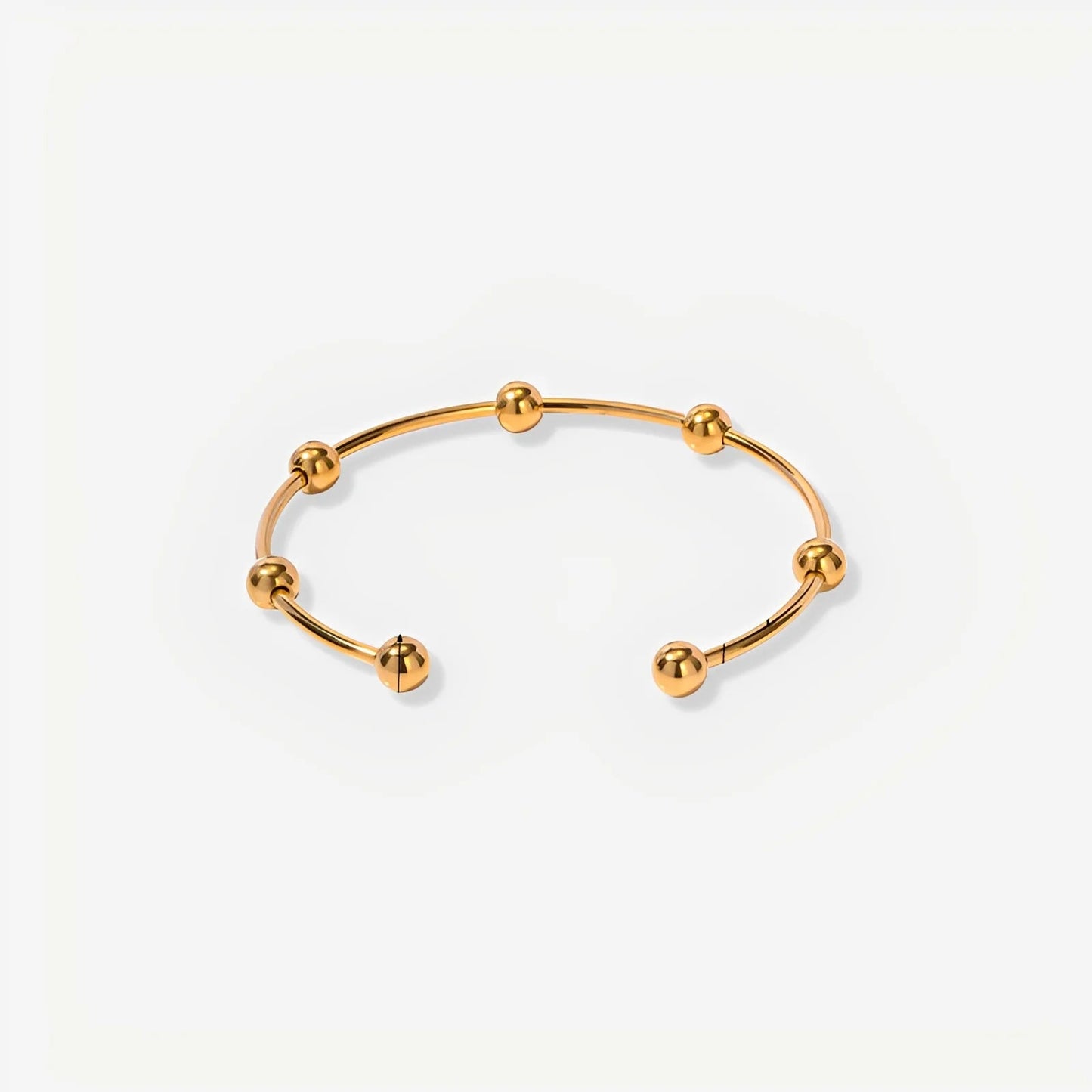 Gold bracelet with spherical ends on a light beige background