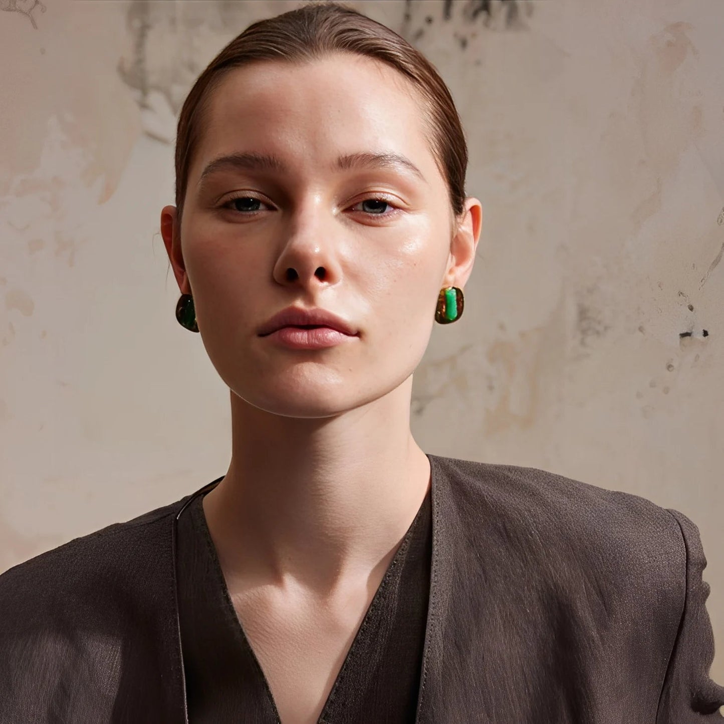 Woman wearing green earrings against a textured beige background