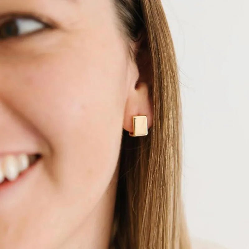Gold square earring worn by a person with a neutral background