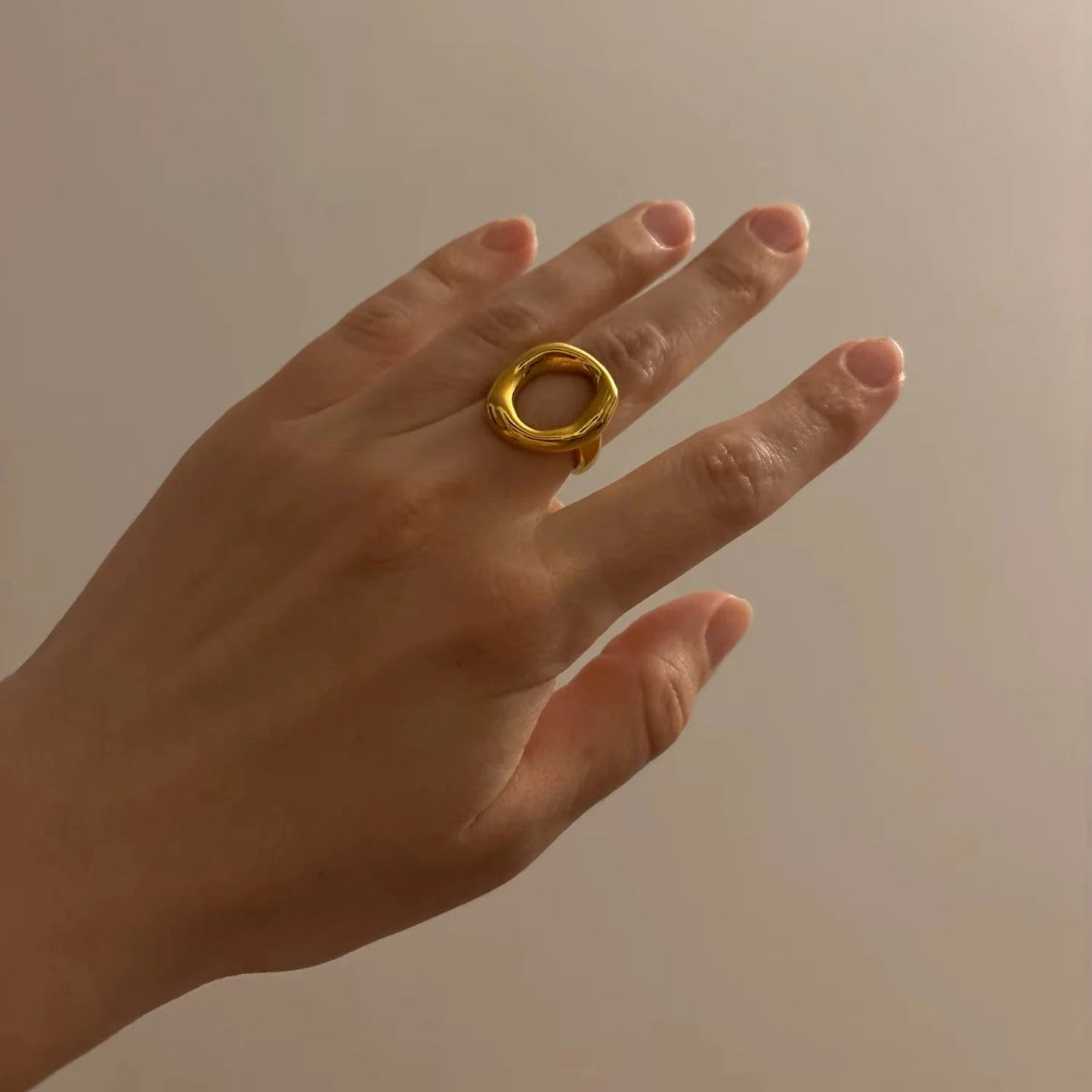 Hand wearing a gold ring against a neutral background