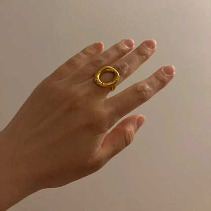 Hand wearing a gold ring against a neutral background