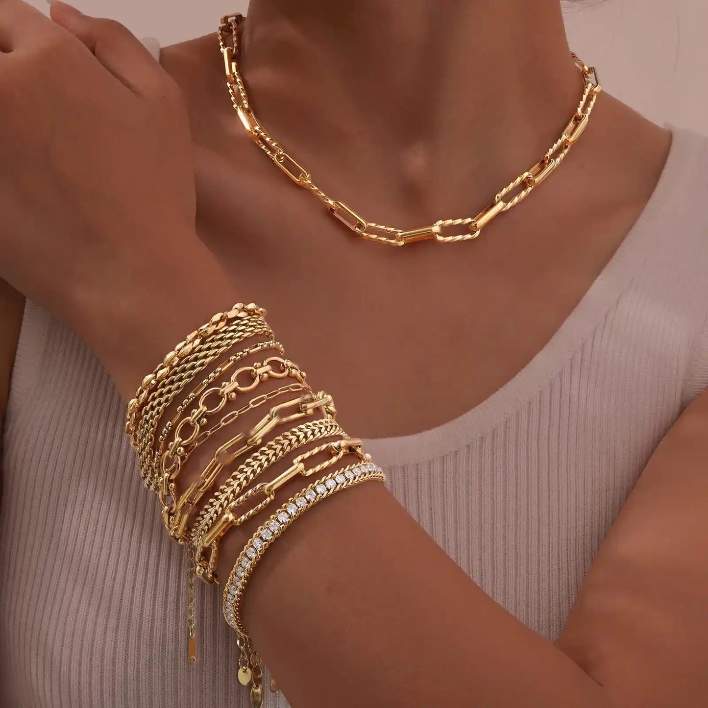 Gold jewelry including a necklace and bracelets on a person's wrist against a neutral background