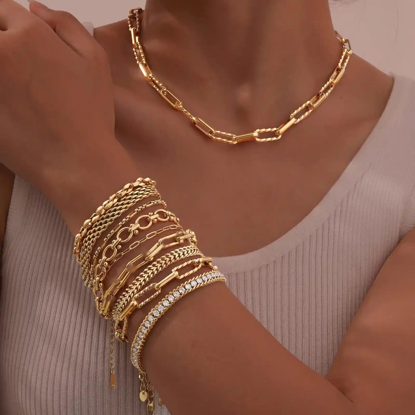 Gold jewelry including a necklace and bracelets on a person's wrist against a neutral background