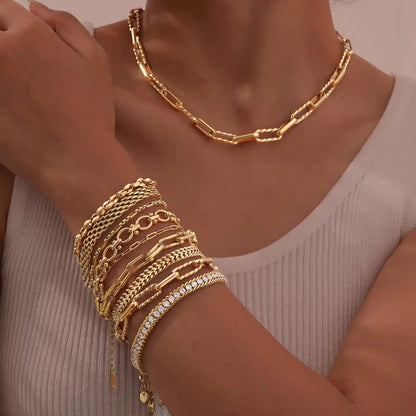 Gold jewelry including a necklace and bracelets on a person's wrist against a neutral background