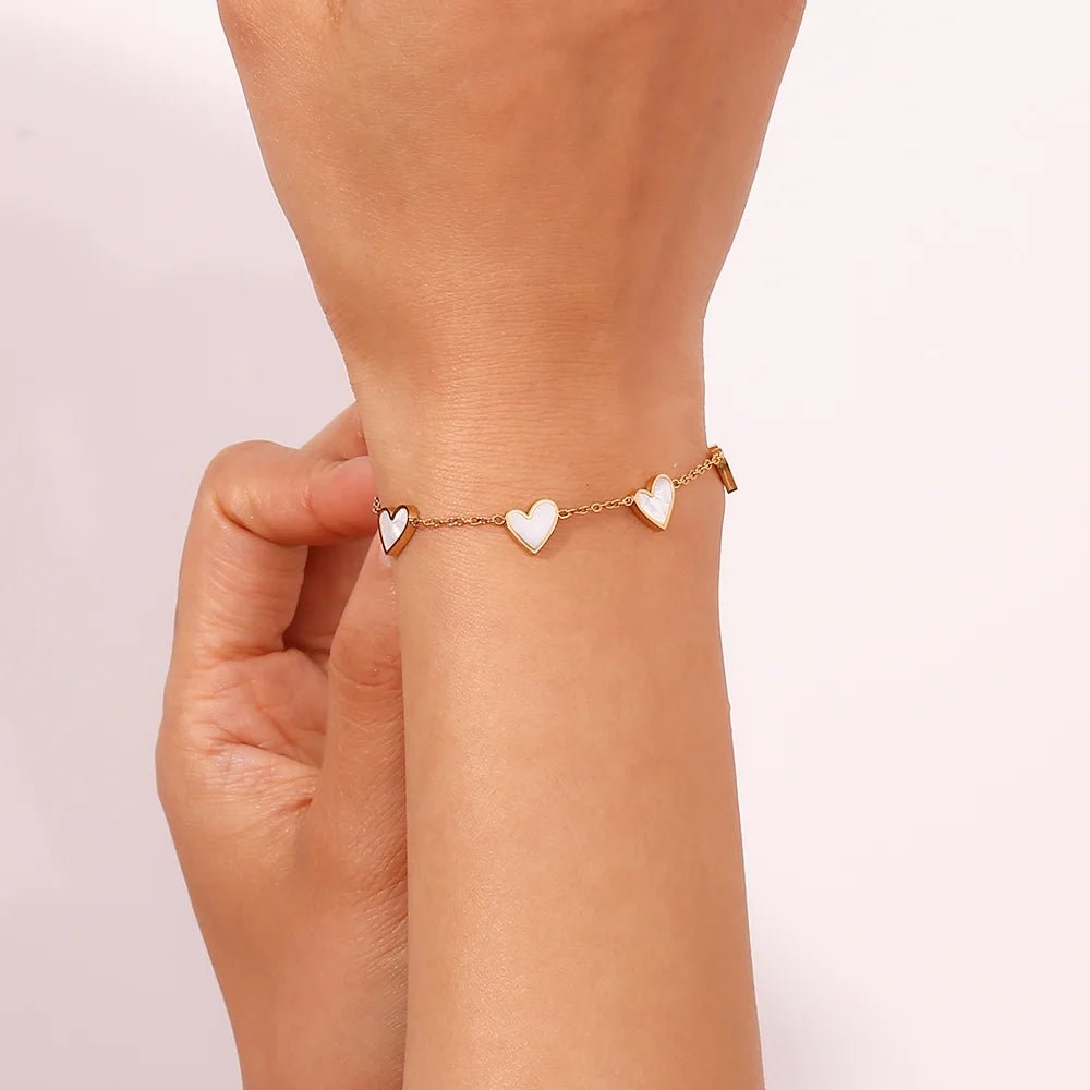 Rose gold bracelet with heart-shaped charms on a wrist against a light pink background