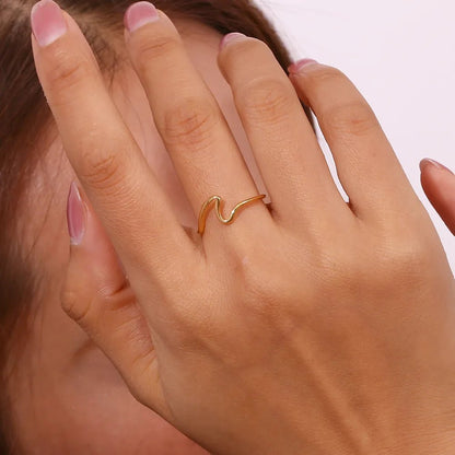 Hand wearing a gold ring with pink nail polish on a neutral background