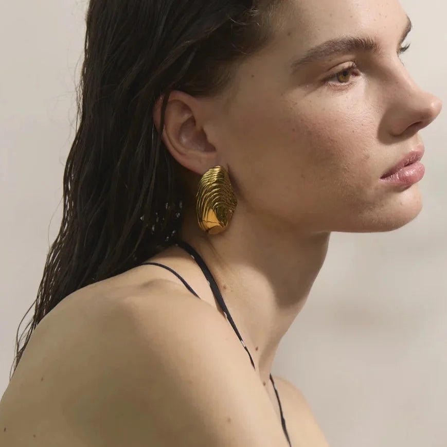 Woman wearing gold earrings with a neutral background