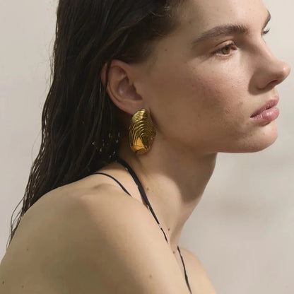 Woman wearing gold earrings with a neutral background