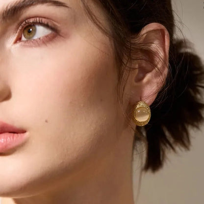 Close-up of a woman wearing a gold earring with a gemstone on a neutral background