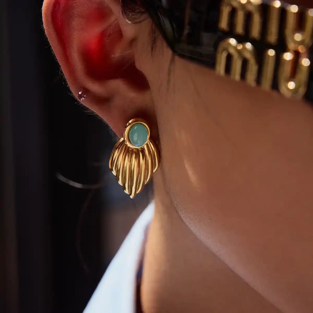 Gold earring with a green gemstone worn by a person, with a blurred background.