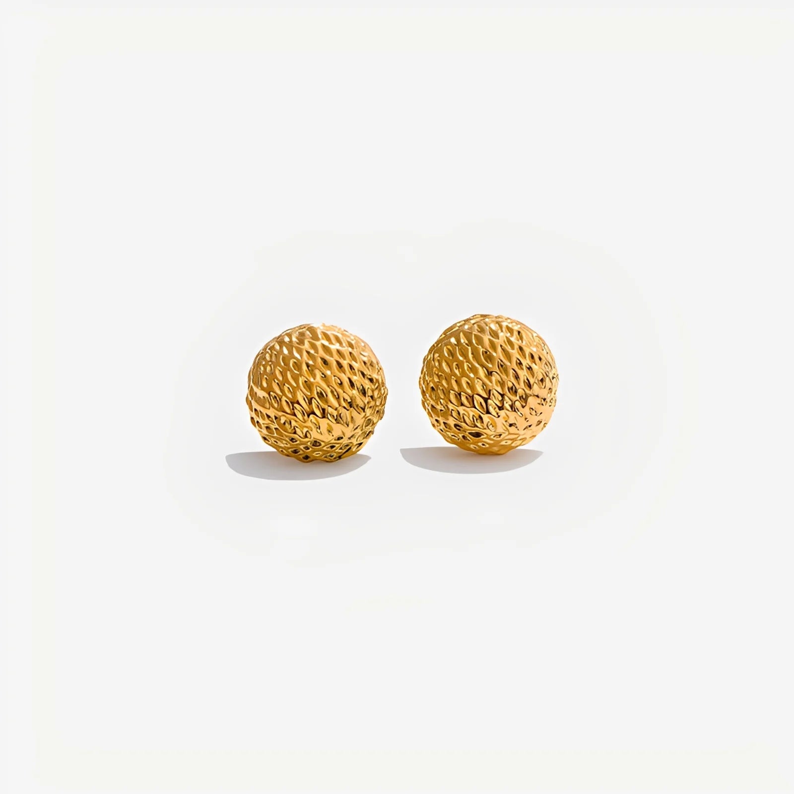 Pair of gold textured sphere earrings on a light gray background