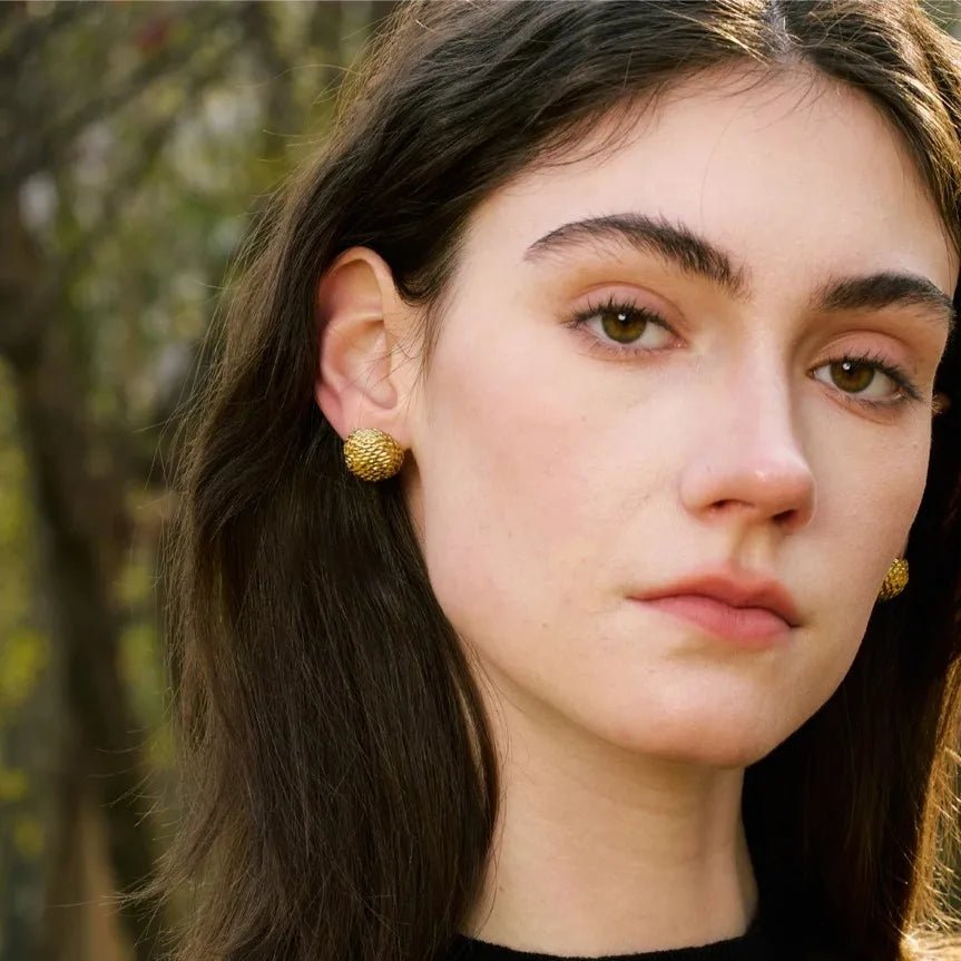 Close-up of a person wearing gold earrings with a blurred natural background