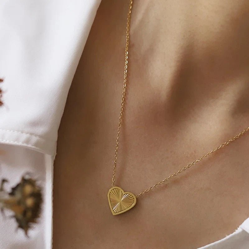Gold heart-shaped necklace on a person wearing a white shirt.