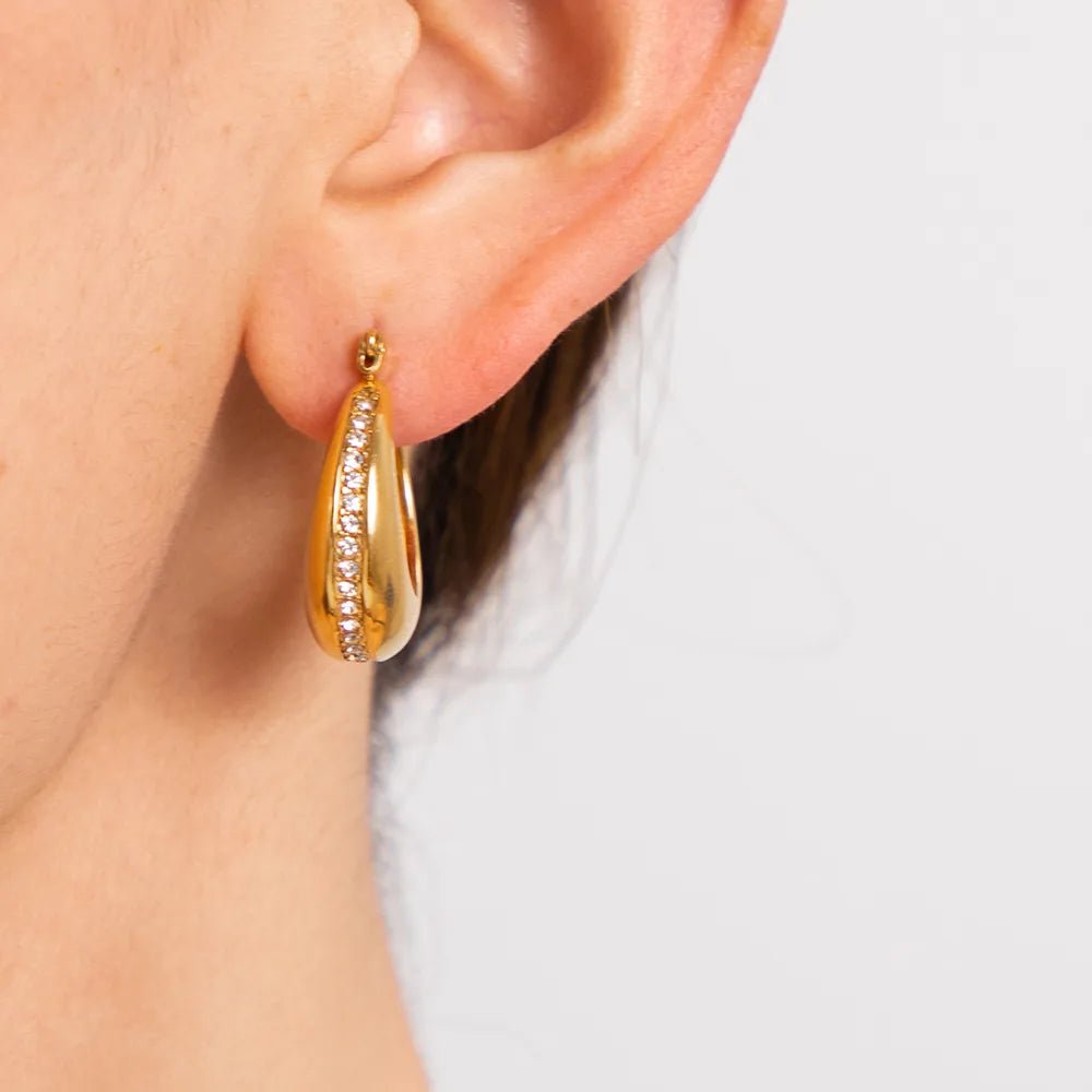 Gold hoop earring worn by a person on a light background