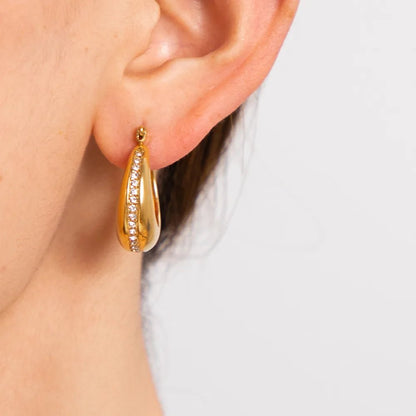 Gold hoop earring worn by a person on a light background
