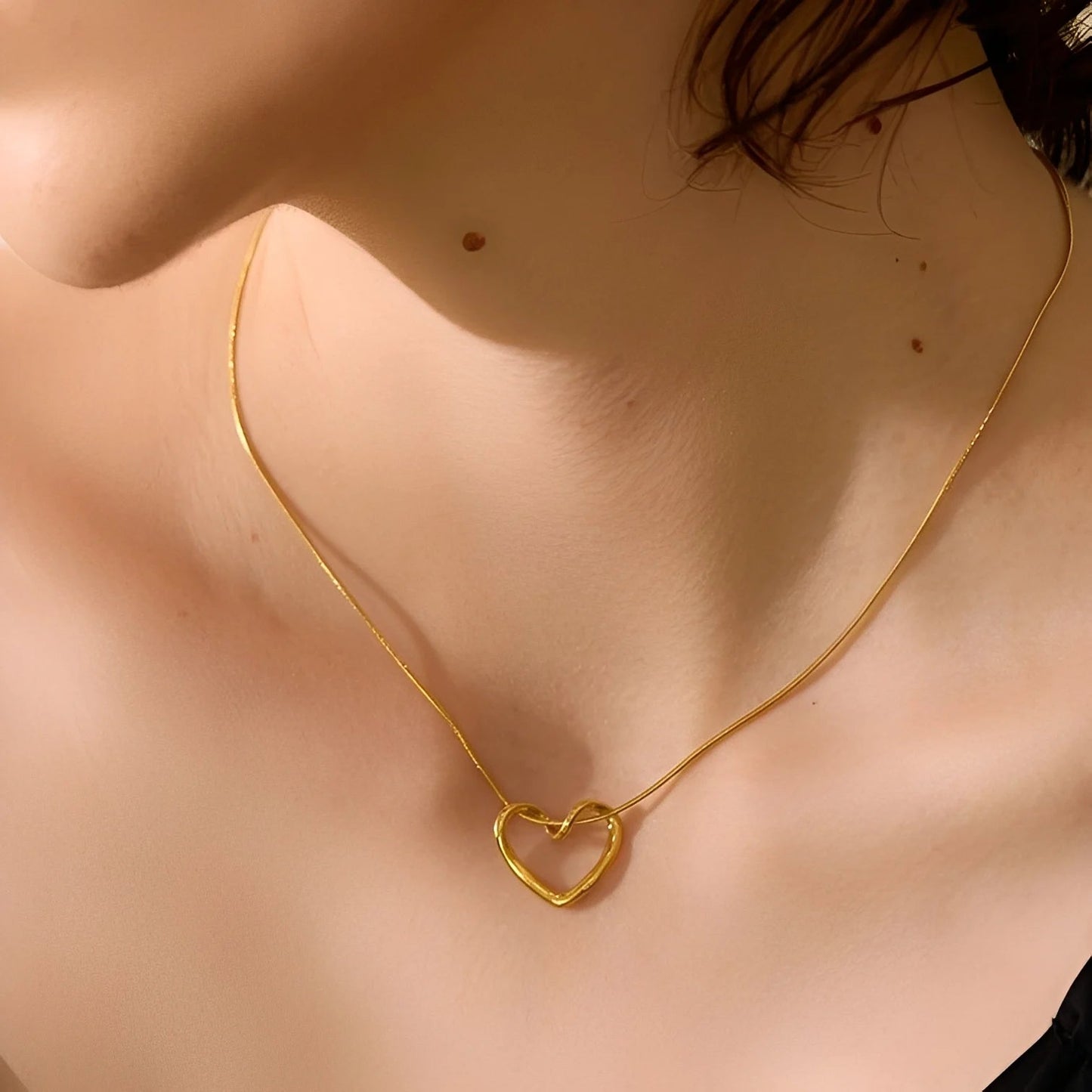 Gold necklace with a heart-shaped pendant on a person's neck