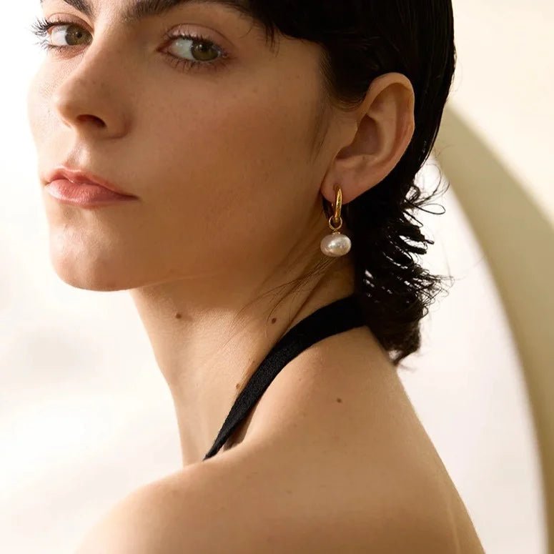 Close-up of a woman wearing pearl earrings with a neutral background