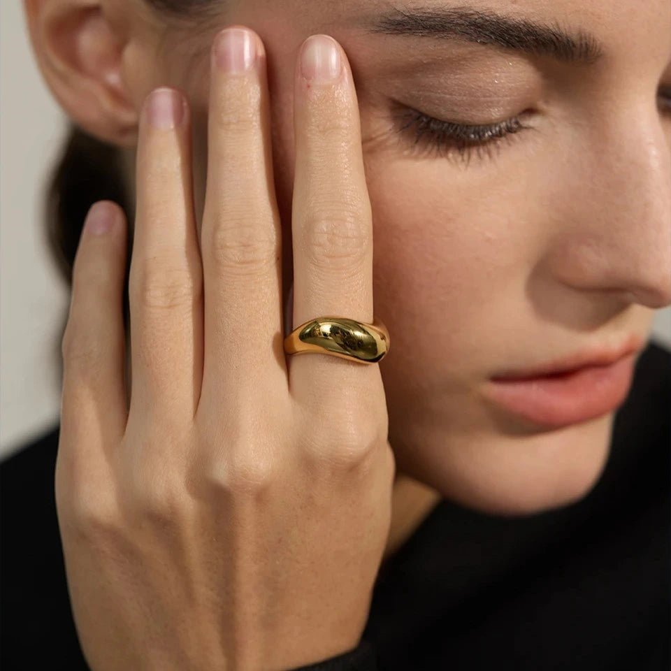 Close-up of a hand with a gold ring on a neutral background