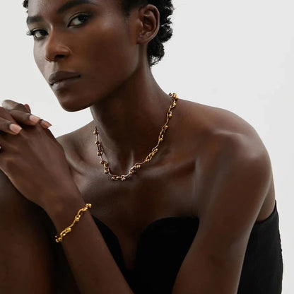 Woman wearing a gold necklace and bracelet against a neutral background
