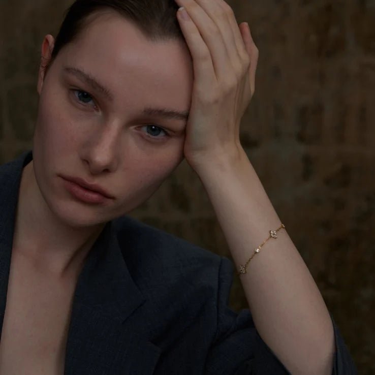Woman with hand on head wearing a gold bracelet against a dark background