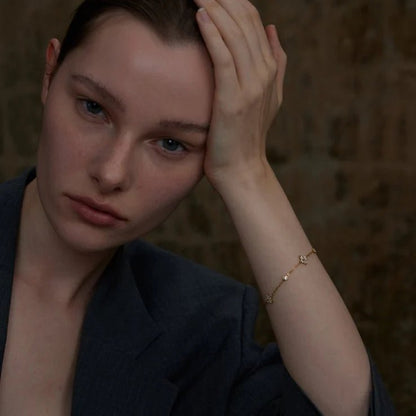 Woman with hand on head wearing a gold bracelet against a dark background