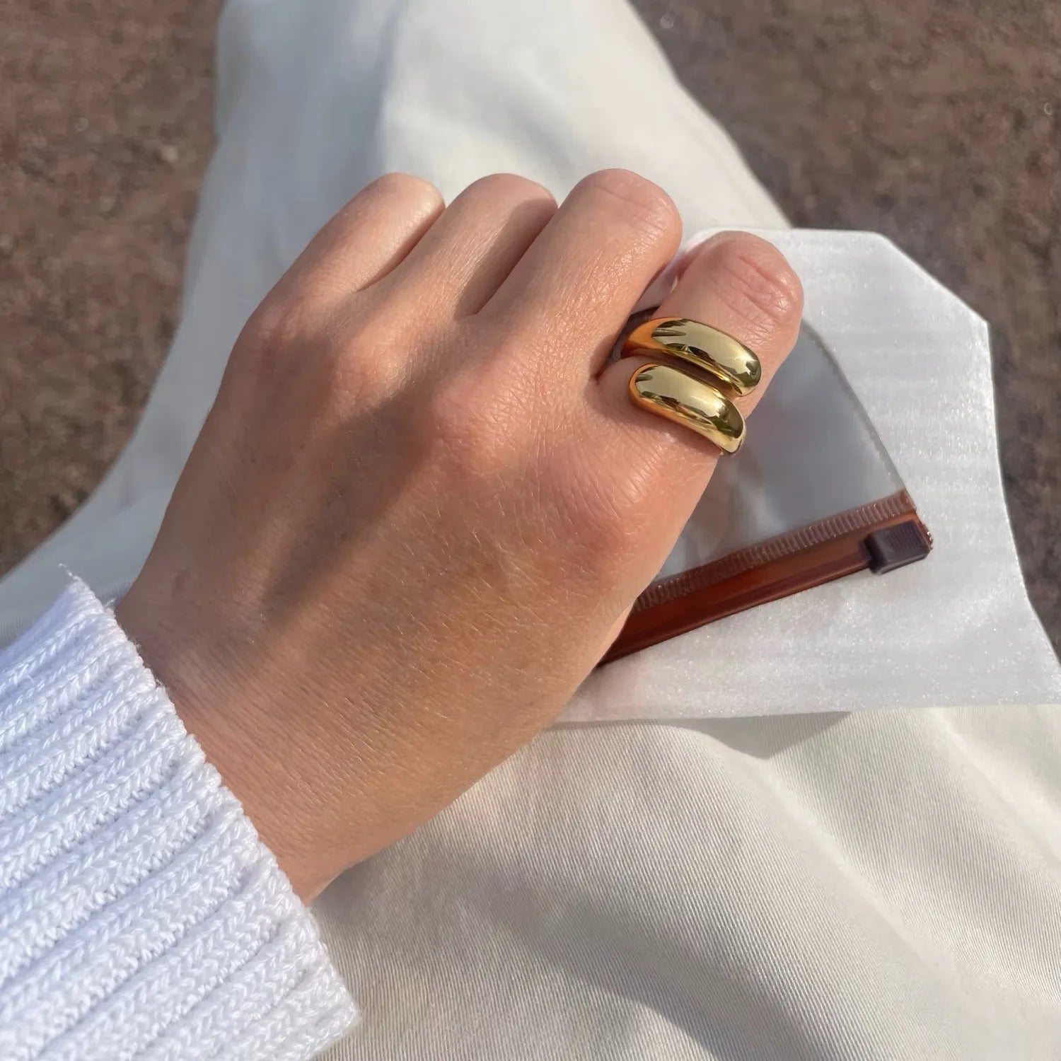 Hand with gold nail polish holding a transparent clutch against a neutral background