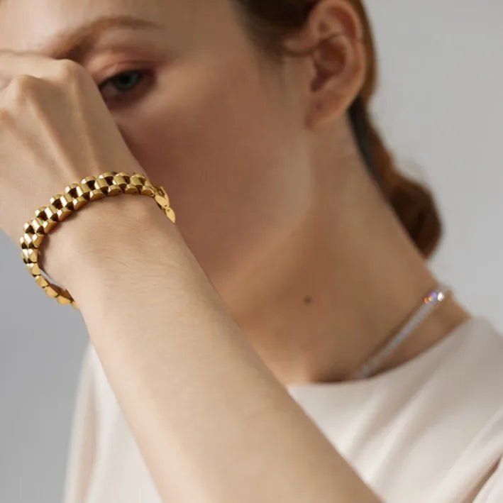 Close-up of a person wearing a gold bracelet on a neutral background