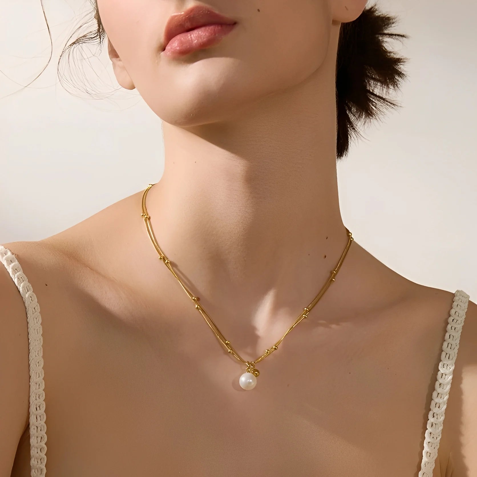 Gold necklace with a pearl pendant worn by a model against a neutral background