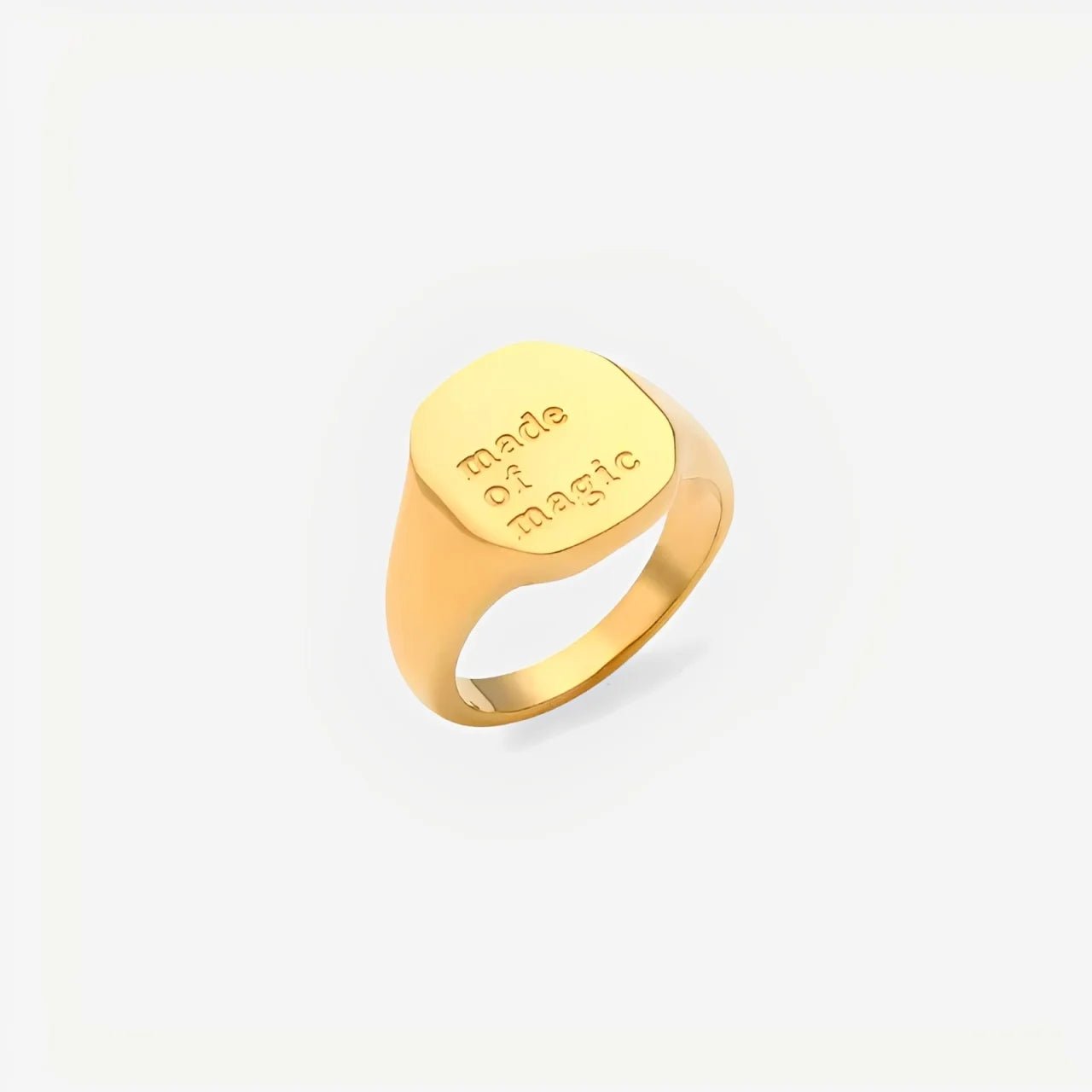 Gold ring with 'Made of magic' engraving on a light beige background