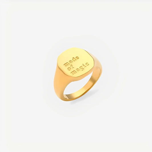 Gold ring with 'Made of magic' engraving on a light beige background