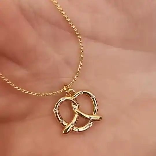 Gold necklace with a double interlocking ring pendant on a soft pink background