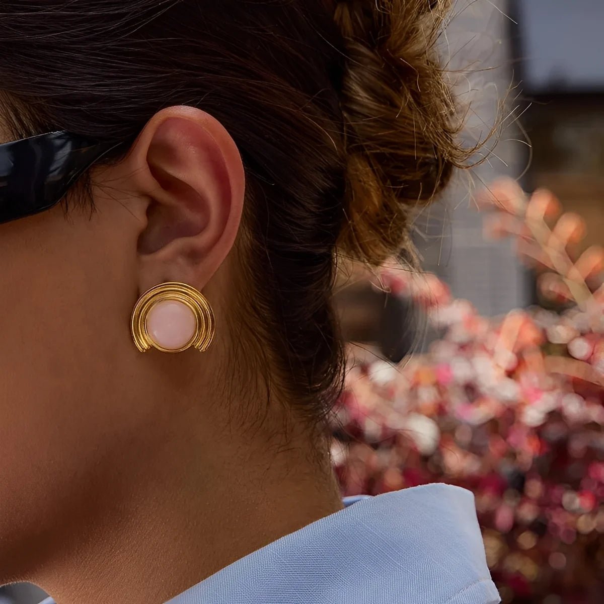 Close-up of a person wearing gold earrings with a blurred colorful background
