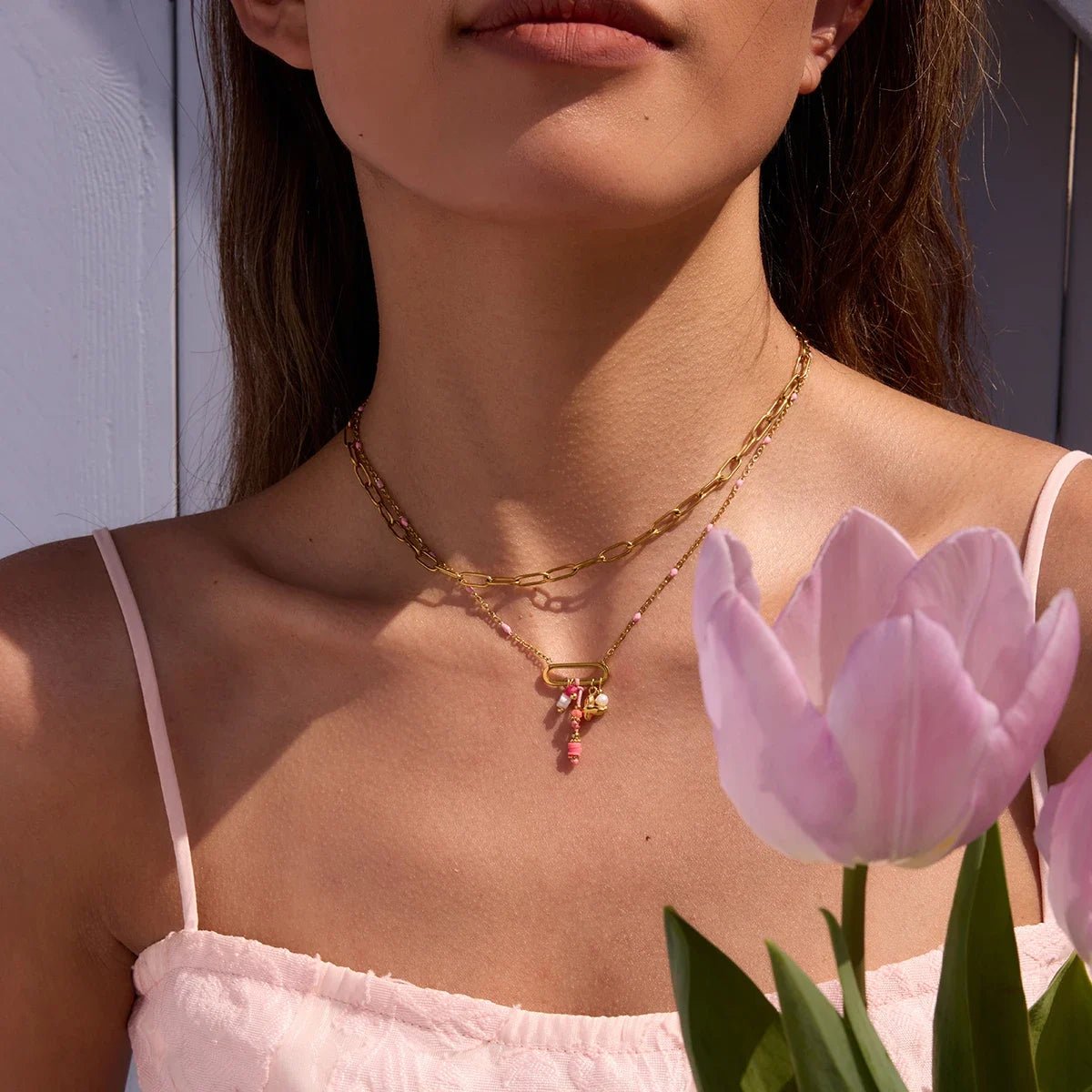 Woman wearing a gold necklace with a pink flower pendant, holding pink tulips.