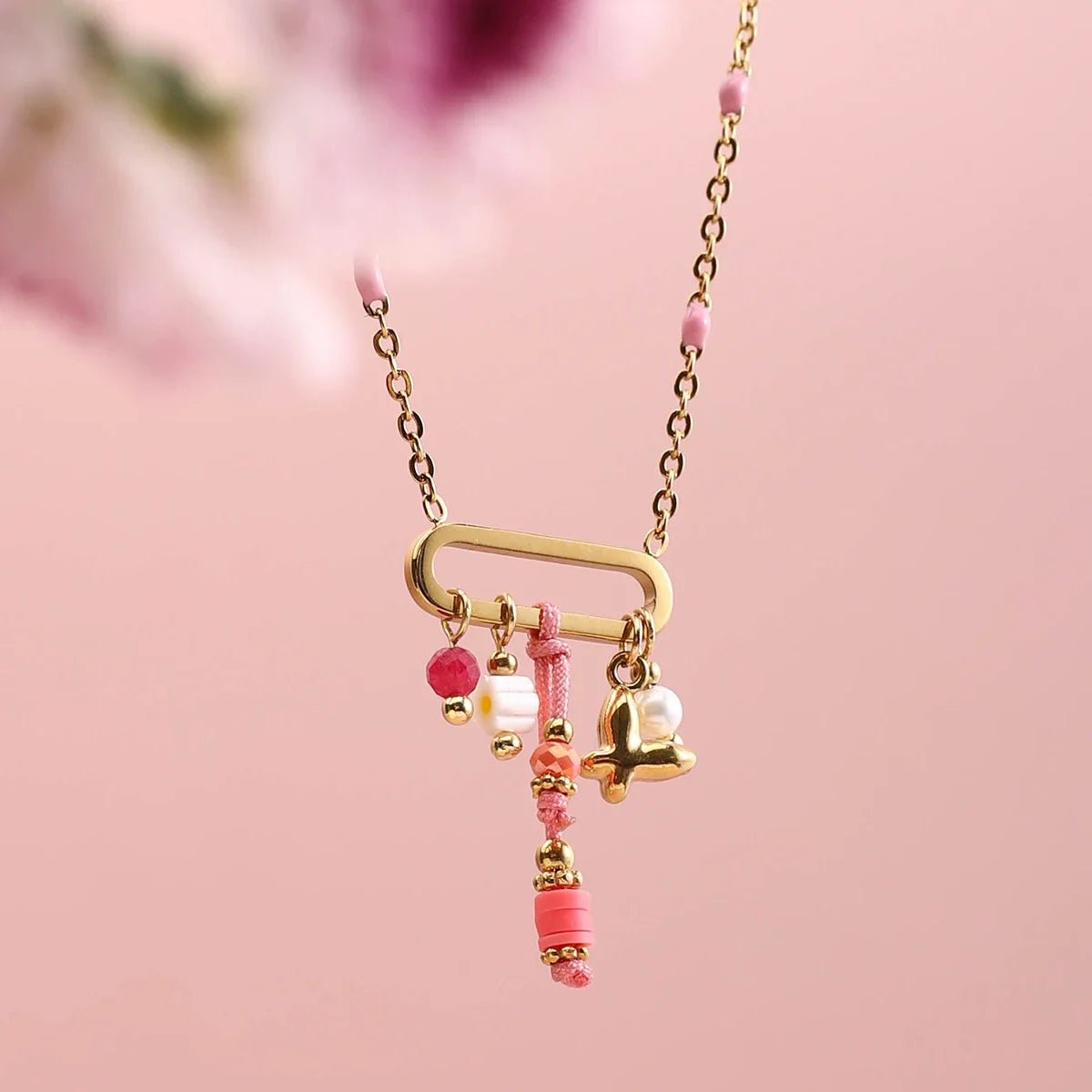 Gold necklace with pink beads and charms on a pink background