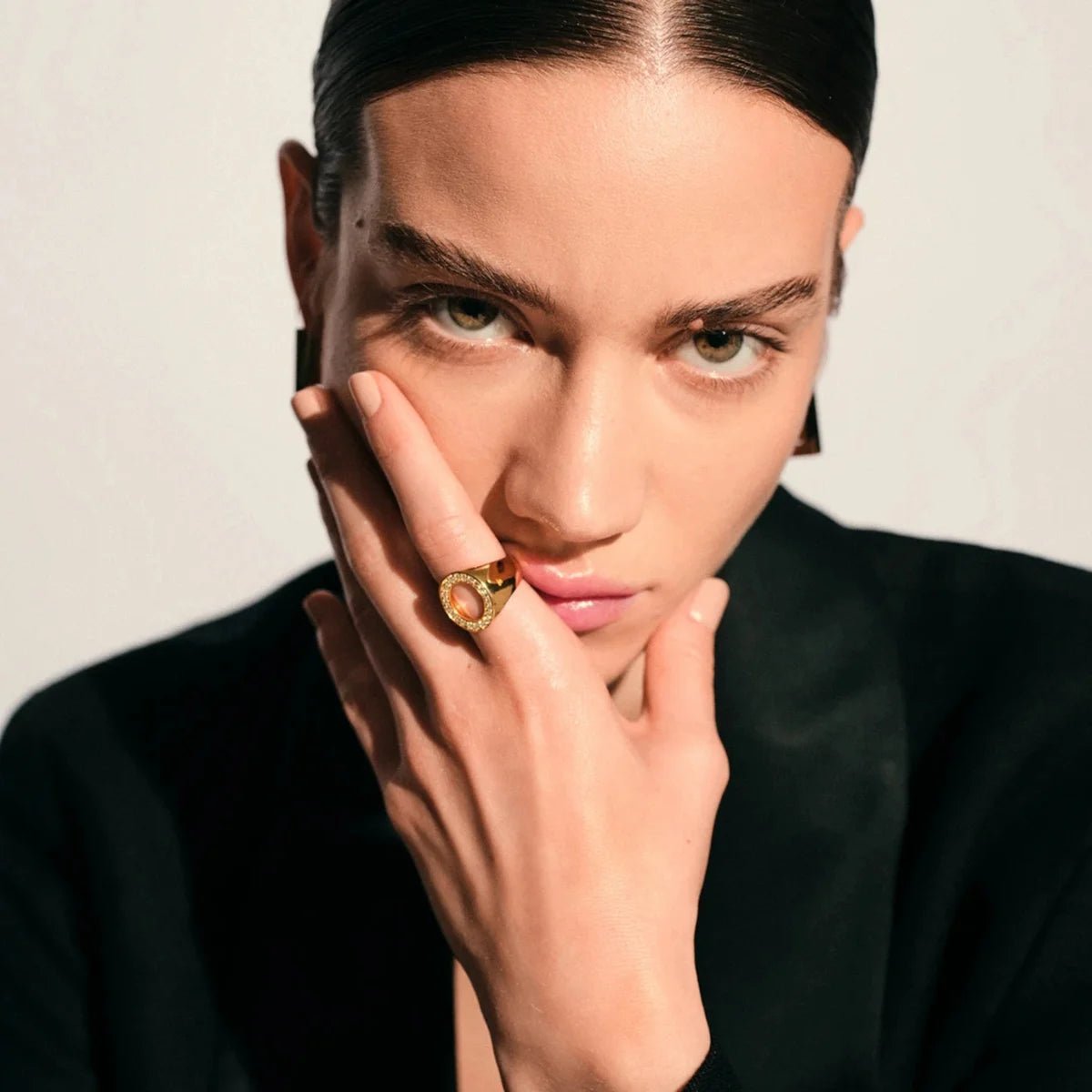 Woman wearing a gold ring on her finger against a neutral background