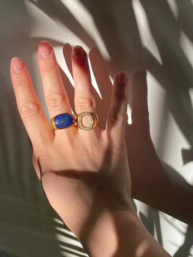Hand wearing two rings with a blue stone and gold band against a light background