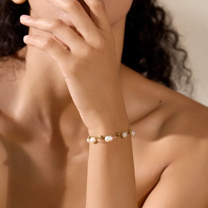 Close-up of a person wearing a gold bracelet with pearls on a blurred background