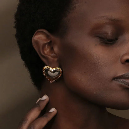 Close-up of a woman wearing a gold heart-shaped earring against a neutral background