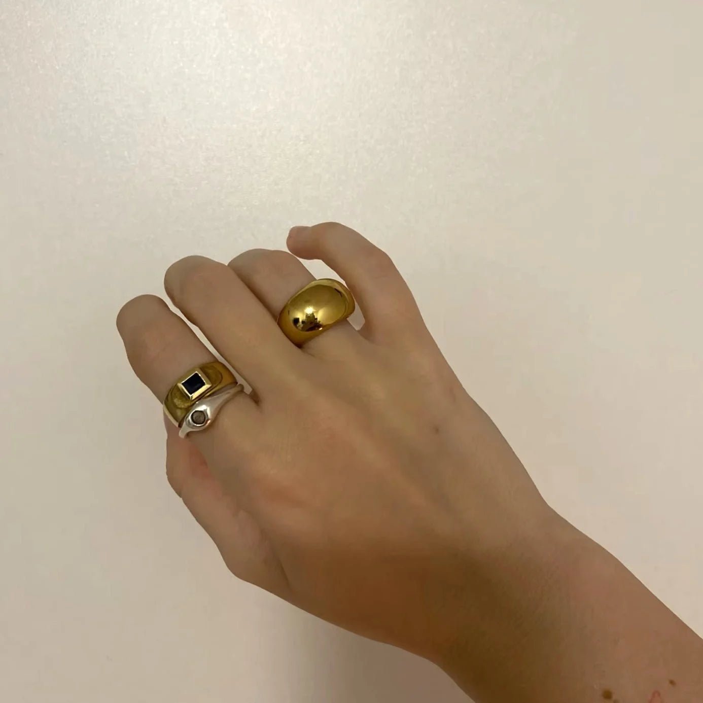 Hand wearing two gold rings against a plain background