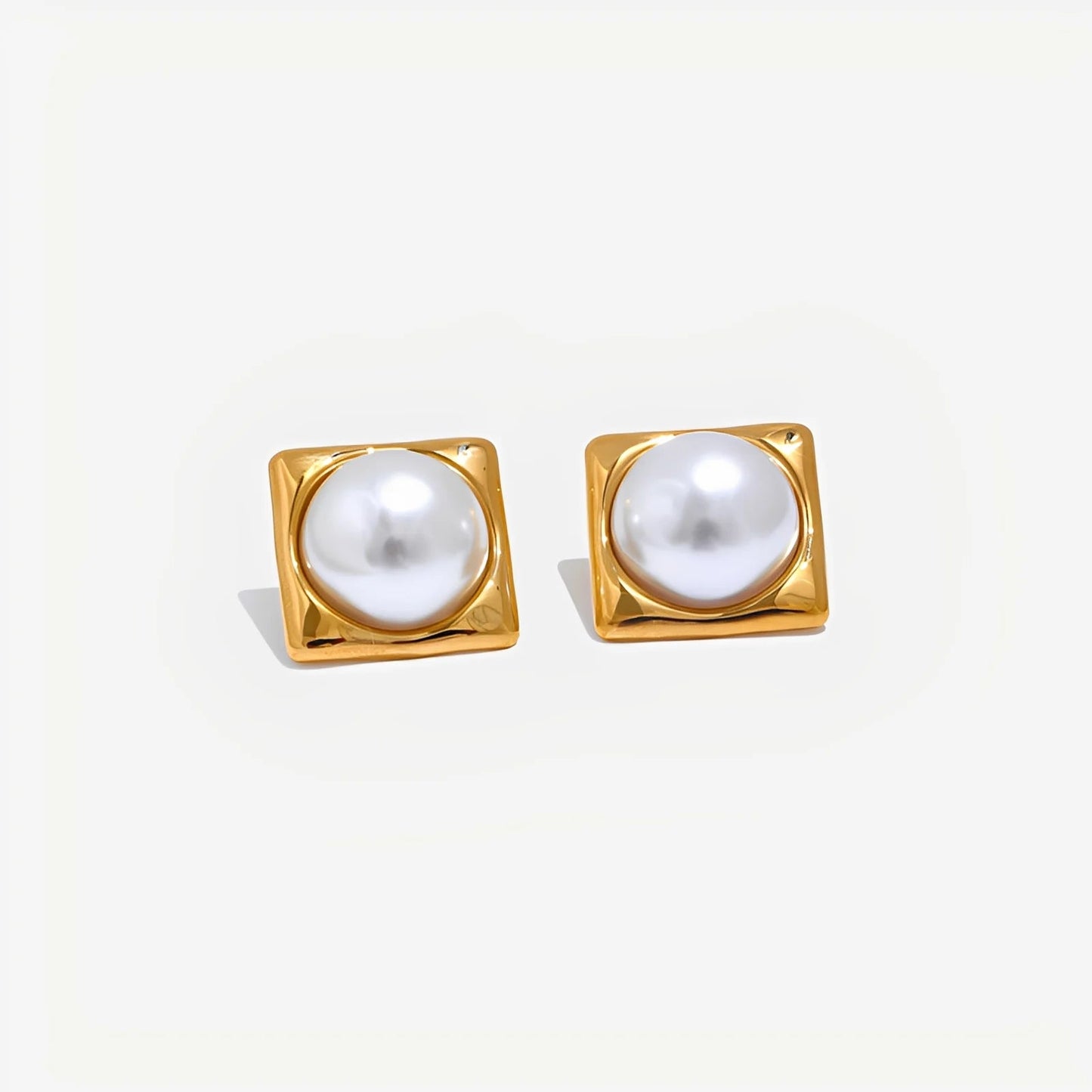 Pair of gold square-framed pearl earrings on a light gray background