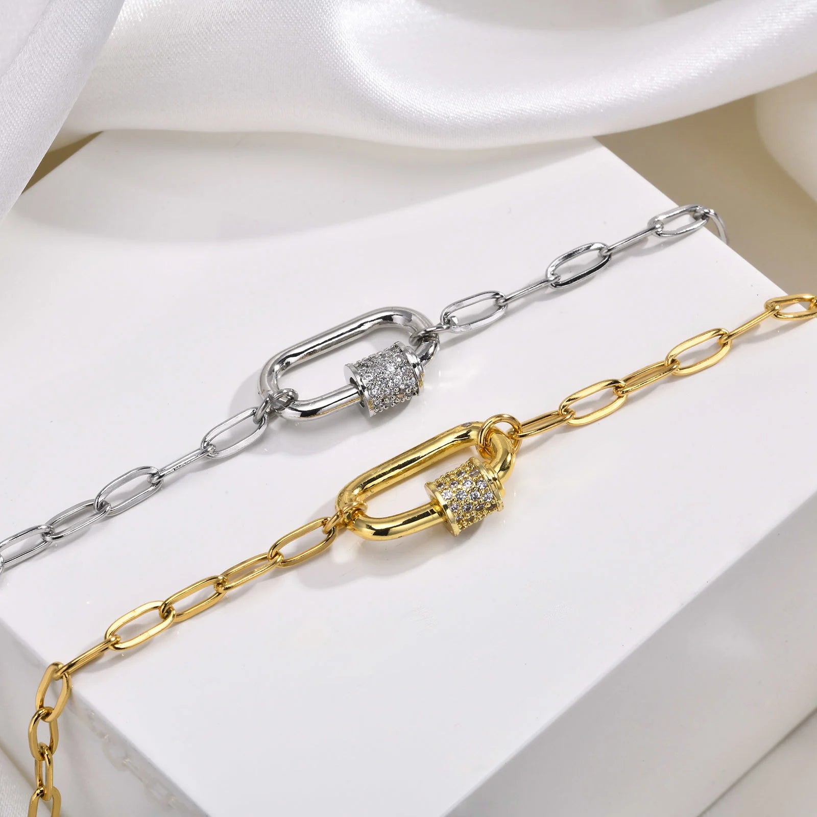 Gold and silver chain necklaces with diamond accents on a white fabric background