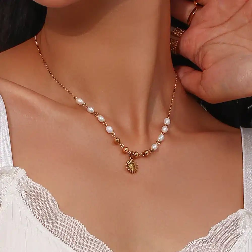 Person wearing a delicate pearl necklace with a sunflower charm.