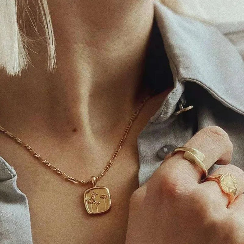 Person wearing a gold necklace and ring with a neutral background